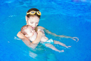 Sweet baby girl enjoying in a pool with her mother, early development class for infants teaching children to swim and dive