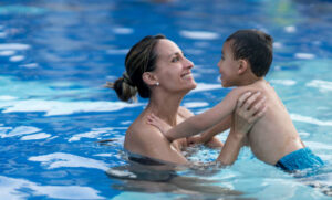 Beautiful young mom holding with excitement her son and holding him in the pool both smiling